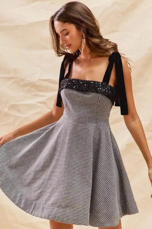 Woman wearing houndstooth fit flare mini dress with black shoulder ties and sequin detail