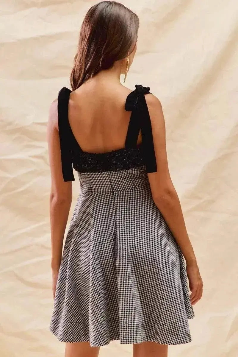 Back view of a woman wearing a houndstooth fit flare mini dress with black shoulder ties.